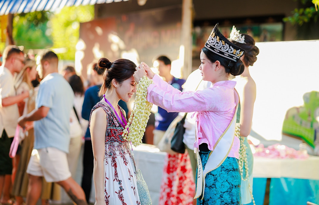 Ambassador in traditional Thai attire presents jasmine garland to visitor at Sky Lanterns Festival, Thailand.