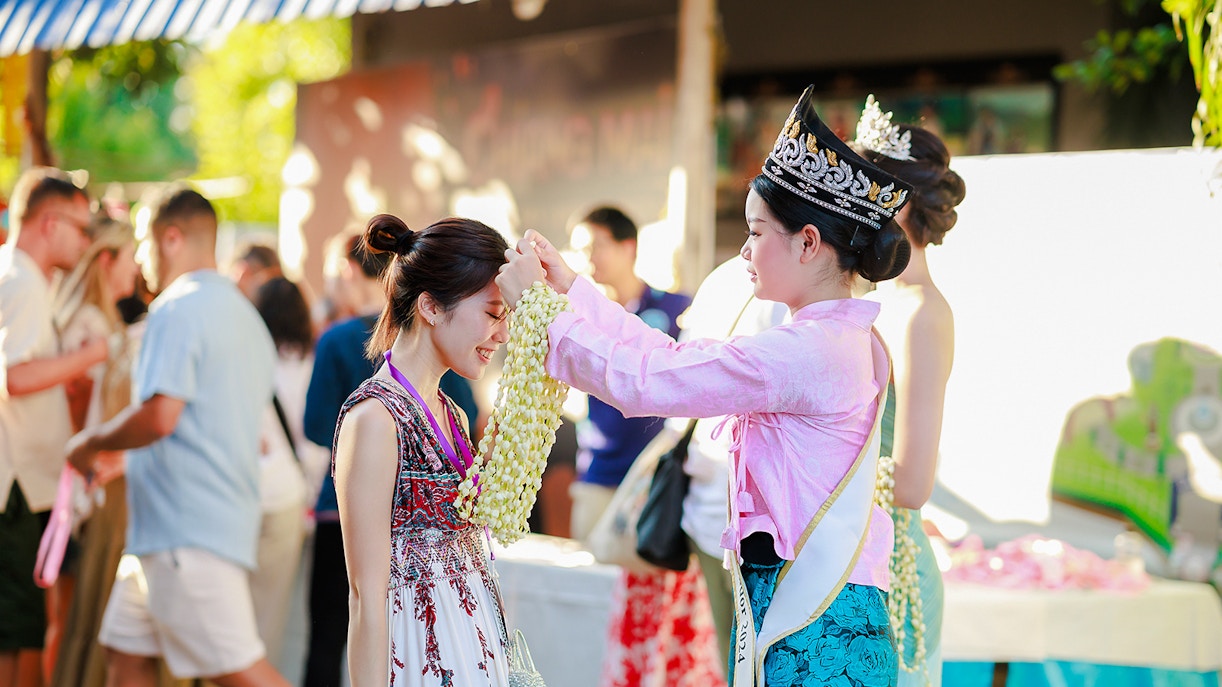 Ambassador in traditional Thai attire presents jasmine garland to visitor at Sky Lanterns Festival, Thailand.