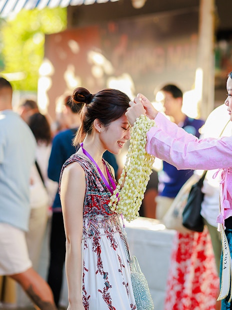 Ambassador in Thai attire presents jasmine garland to visitor at Sky Lanterns Festival.