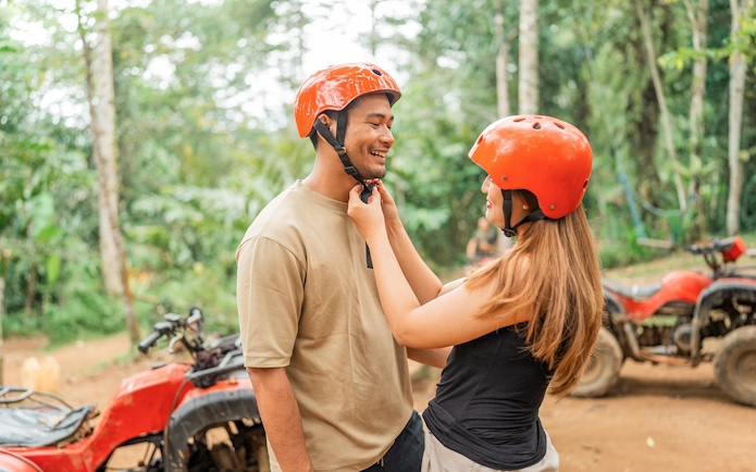 Couple preparing for ATV ride in Phuket jungle with helmets.