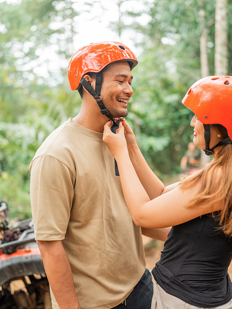 Couple preparing for ATV ride in Phuket jungle with helmets.