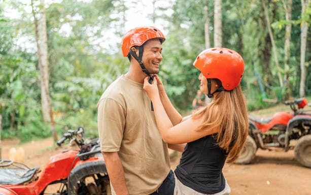Couple preparing for ATV ride in Phuket jungle with helmets.