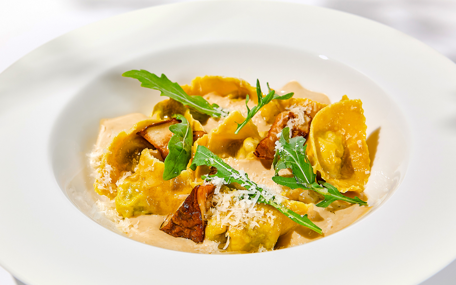 Italian ravioli with meat and mushroom sauce, garnished with arugula and cheese.