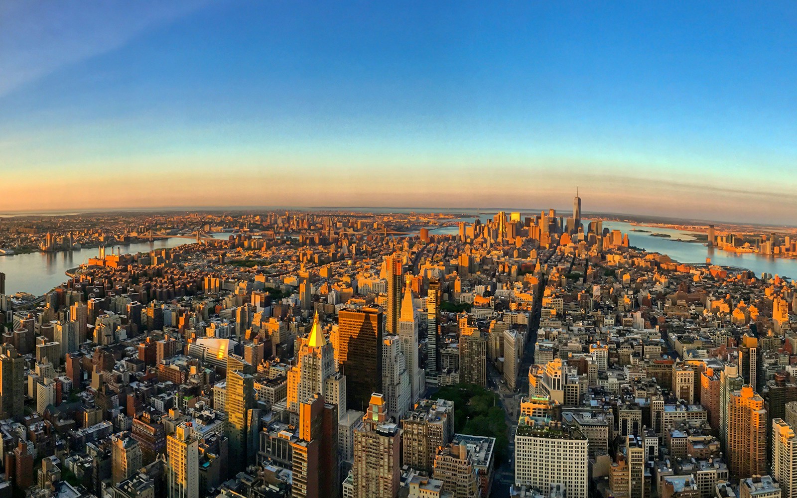 Aerial view of New York City skyline at sunrise from 86th floor, featuring iconic skyscrapers and rivers.