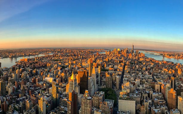 Aerial view of New York City skyline at sunrise from 86th floor, featuring iconic skyscrapers and rivers.