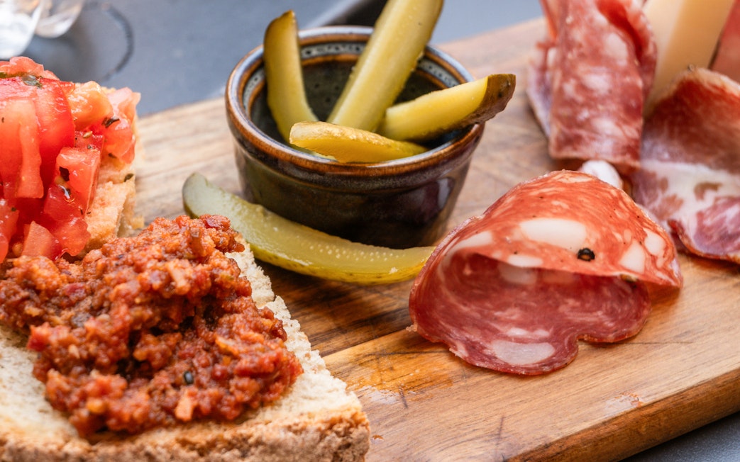 Pisan specialties with bruschetta, salami, and pickles on a wooden board during Pisa guided tour.