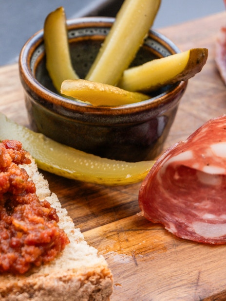 Pisan specialties with bruschetta, salami, and pickles on a wooden board during Pisa guided tour.