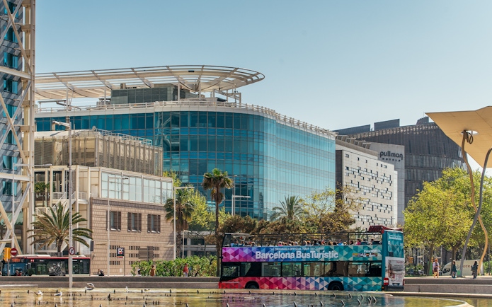 Barcelona tour bus in front of modern buildings on a sunny day.