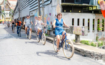 Cyclists riding through Bangkok street near temple on bicycle tour.