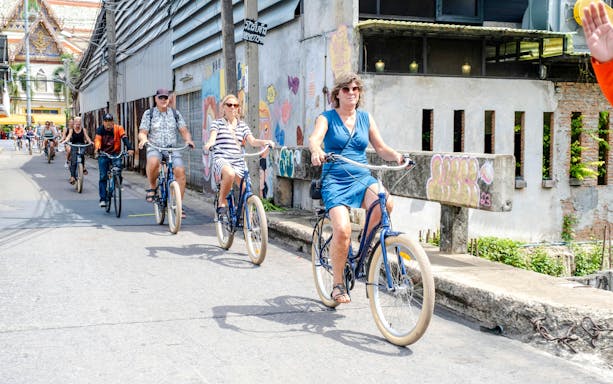 Cyclists riding through Bangkok street near temple on bicycle tour.