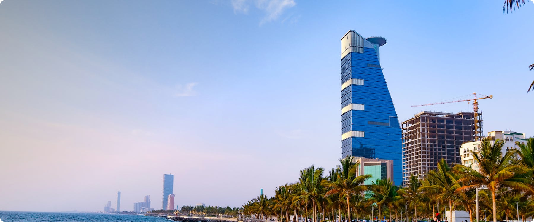 Jeddah waterfront with modern skyscraper and palm-lined promenade.