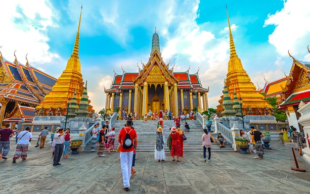 Visitors exploring Bangkok's Grand Palace with golden spires and ornate architecture on a guided tour.