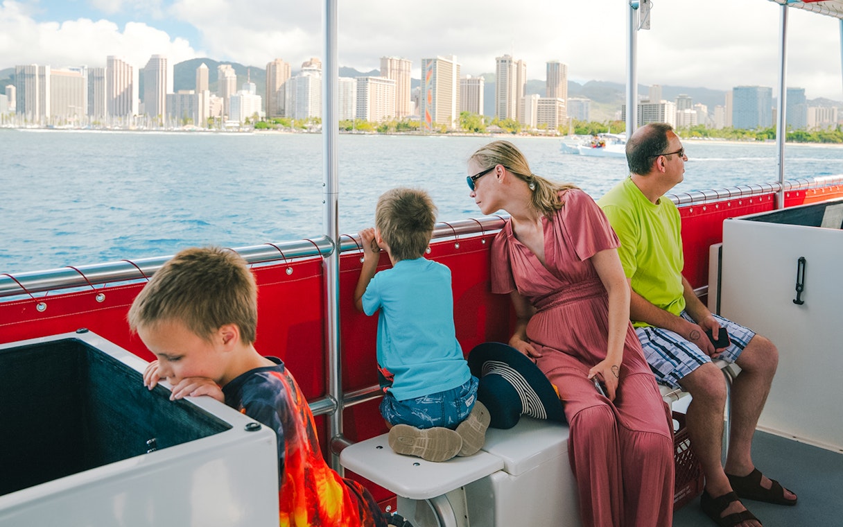 Guests on a Hawaii glass-bottom boat tour with Honolulu skyline in the background.