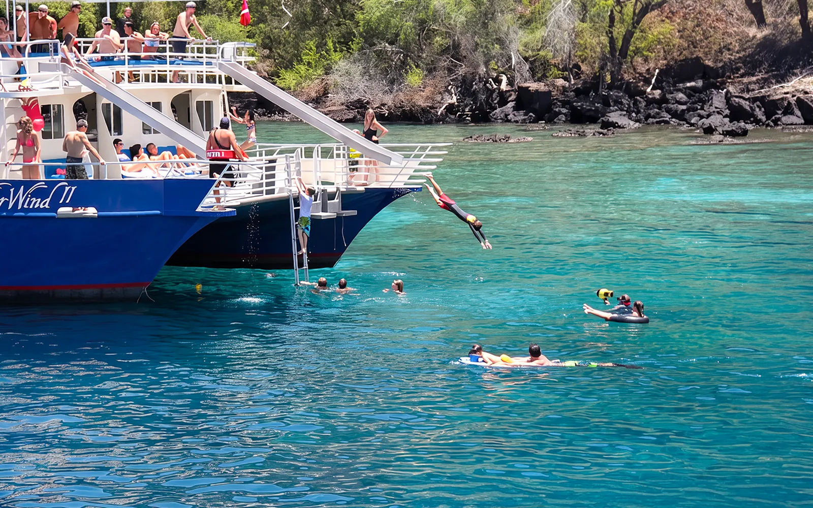 Snorkelers and divers enjoy Kealakekua Bay from a boat in clear blue water.