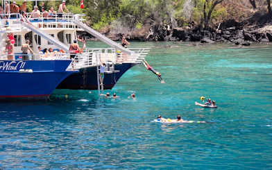 Snorkelers and divers enjoy Kealakekua Bay from a boat in clear blue water.