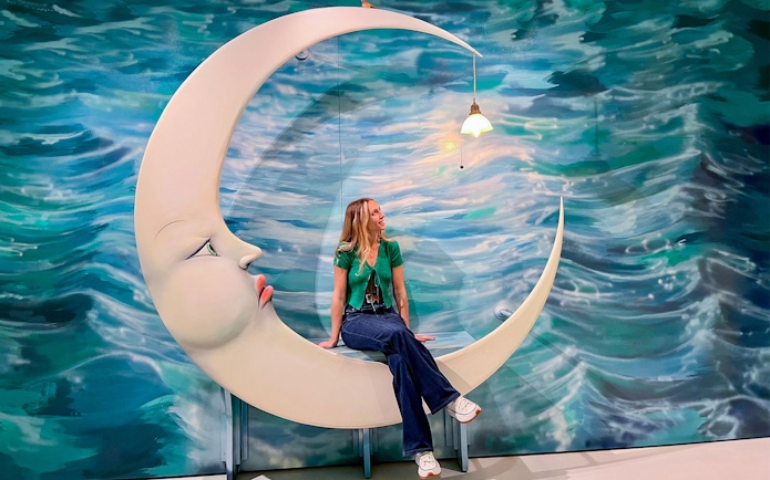 Visitor sitting on crescent moon sculpture at Moco Museum, Barcelona.