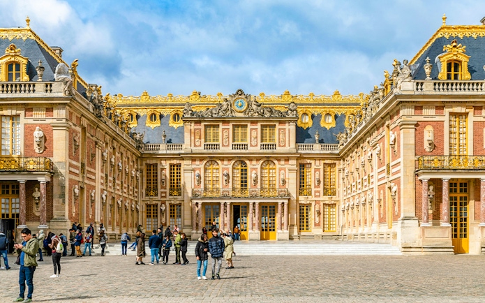 Palace of Versailles courtyard with visitors, showcasing ornate architecture and golden details.