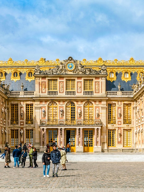 Palace of Versailles courtyard with visitors, showcasing ornate architecture and golden details.