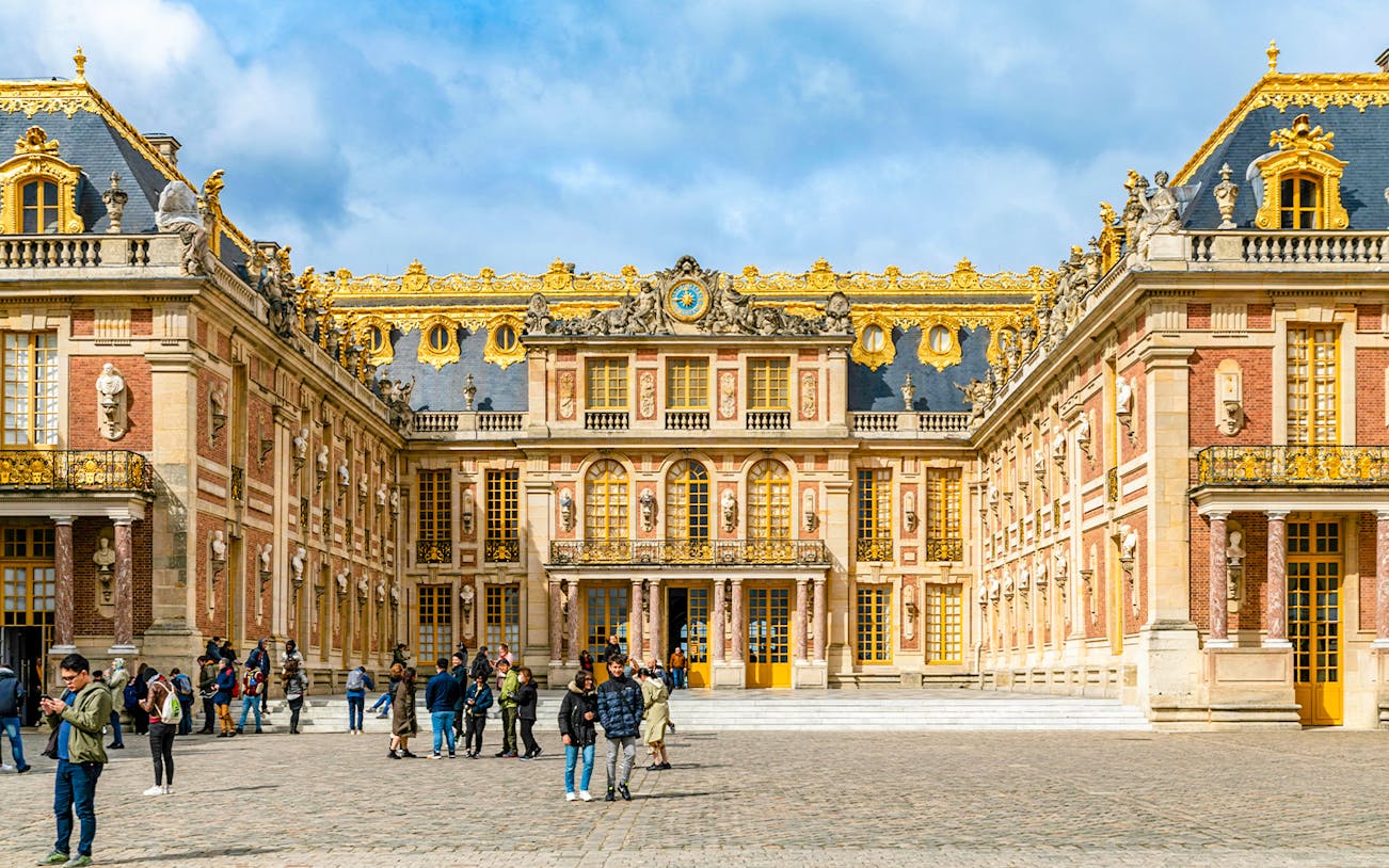 Palace of Versailles courtyard with visitors, showcasing ornate architecture and golden details.