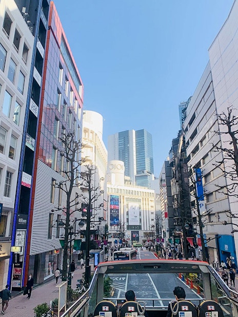 Tokyo street view from Sky Hop Bus on a sunny day, showcasing modern buildings and bustling sidewalks.