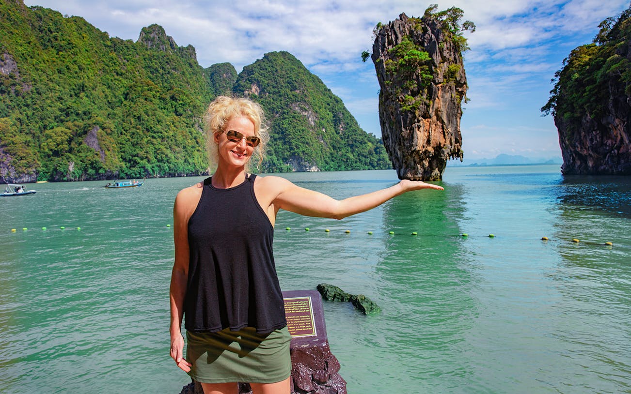 Woman posing with James Bond Island in Phang Nga Bay during sunset cruise.