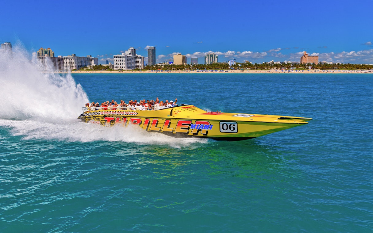 Speedboat with tourists on Miami sightseeing tour, city skyline in background.