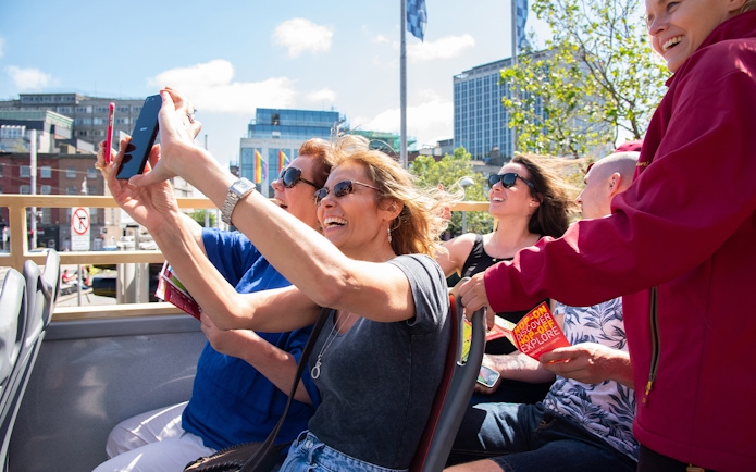Tourists enjoying a Dublin Explorer Pass bus tour, taking photos and holding guidebooks.