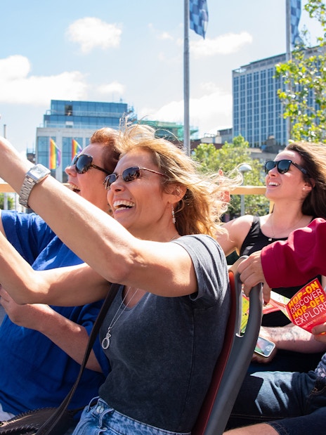 Tourists enjoying a Dublin Explorer Pass bus tour, taking photos and holding guidebooks.