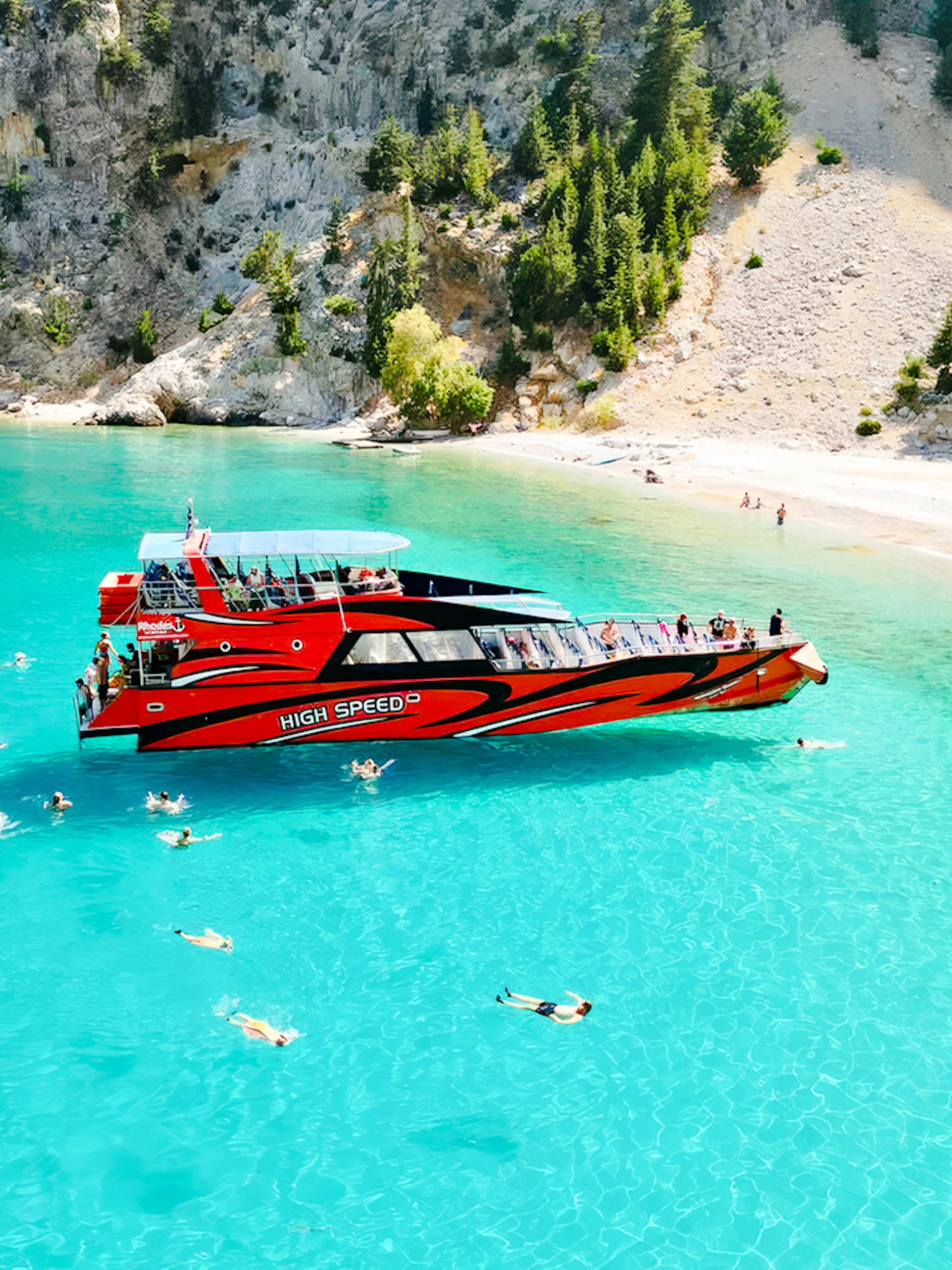 Tourists swimming near a red boat in St George's Bay, Rhodes.