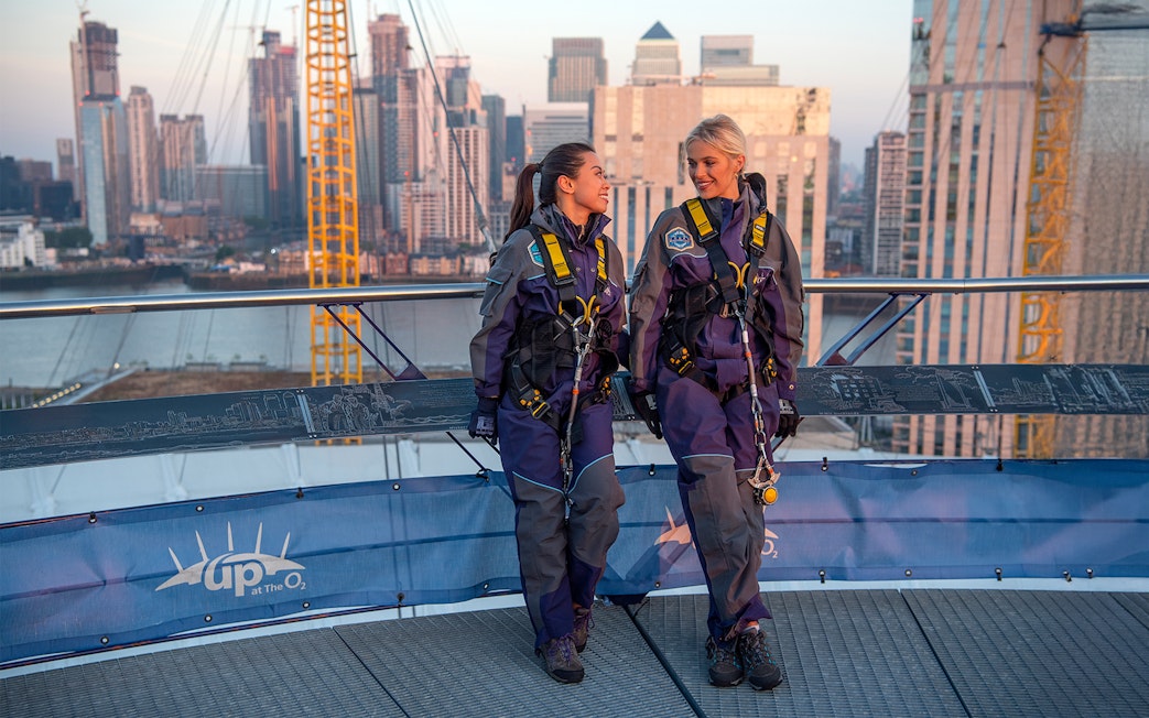 Guests in climbing gear at the O2 Arena rooftop during sunset in London.