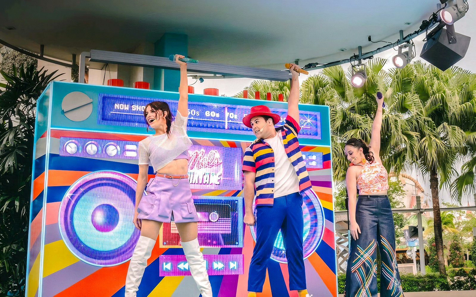 Performers on stage with a colorful backdrop, singing hits from various decades at Universal.