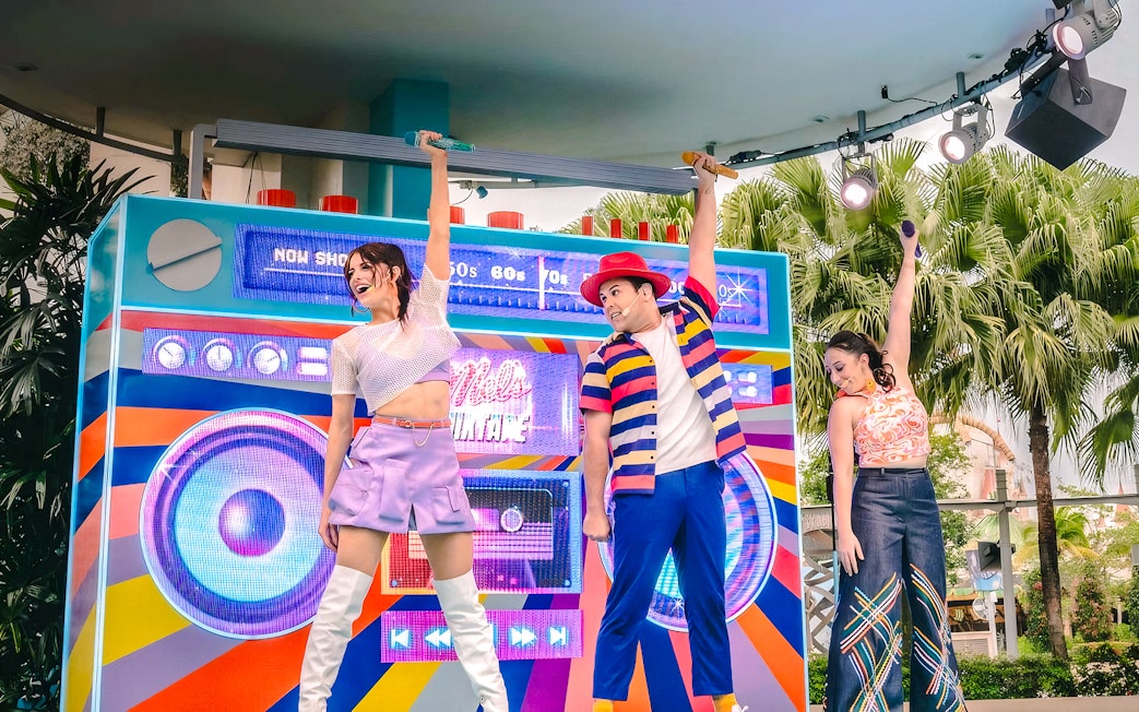 Performers on stage with a colorful backdrop, singing hits from various decades at Universal.