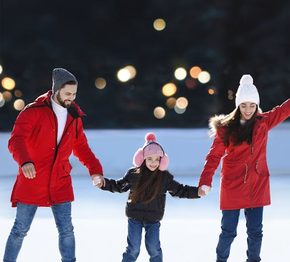 Family ice skating together at an outdoor rink.