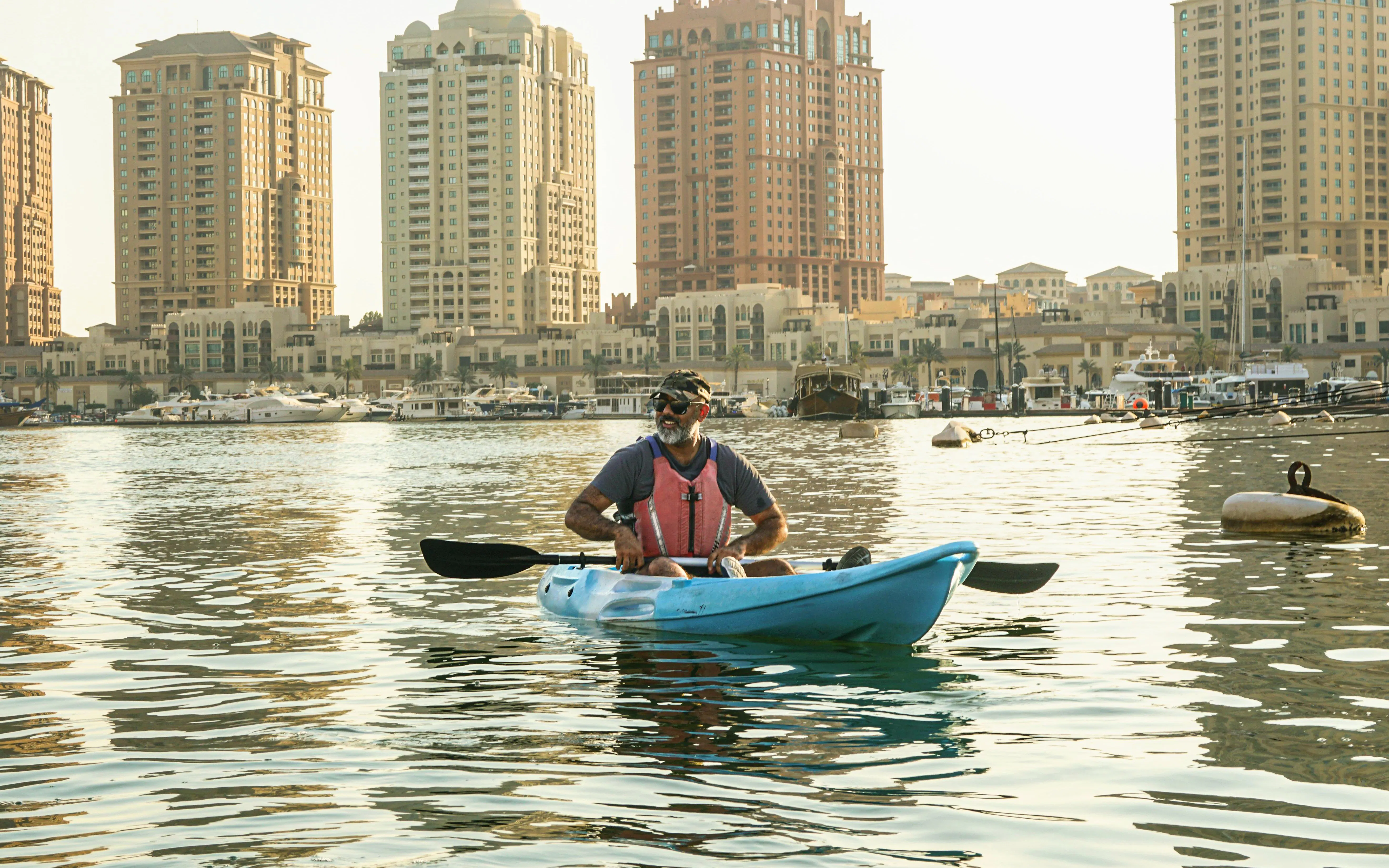 Kayaker paddling in The Pearl, Doha with city skyline in the background.