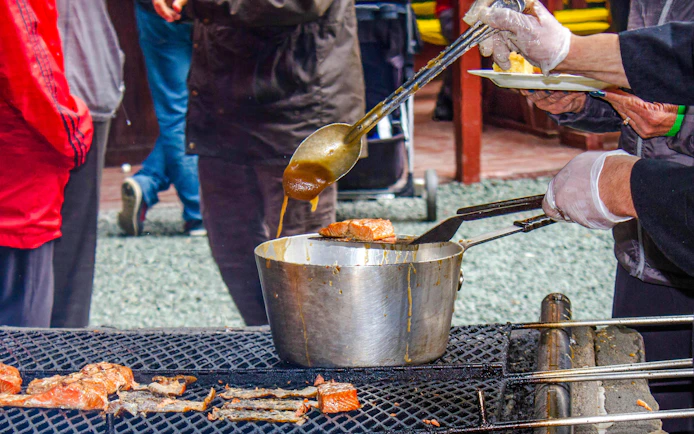 Salmon being grilled and basted at an outdoor salmon bake event.