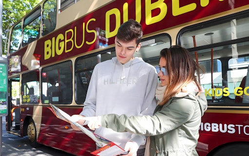 Tourists with a map in front of a Dublin sightseeing bus.