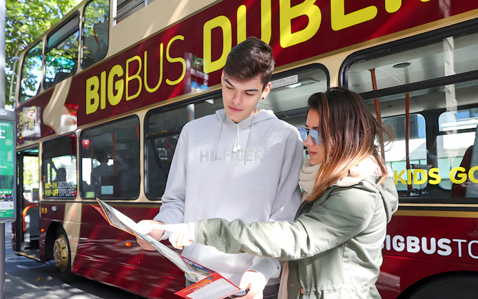 Tourists with a map in front of a Dublin sightseeing bus.