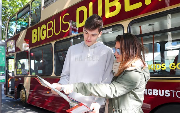 Tourists with a map in front of a Dublin sightseeing bus.