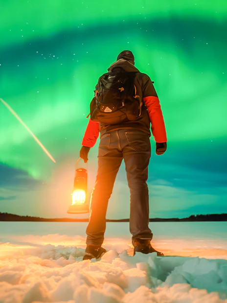 Person holding lantern under Northern Lights in Rovaniemi.