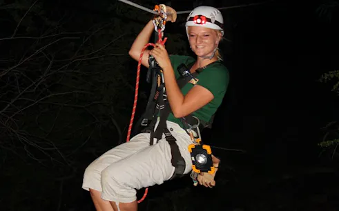Nighttime ziplining adventure with headlamp in forest setting.