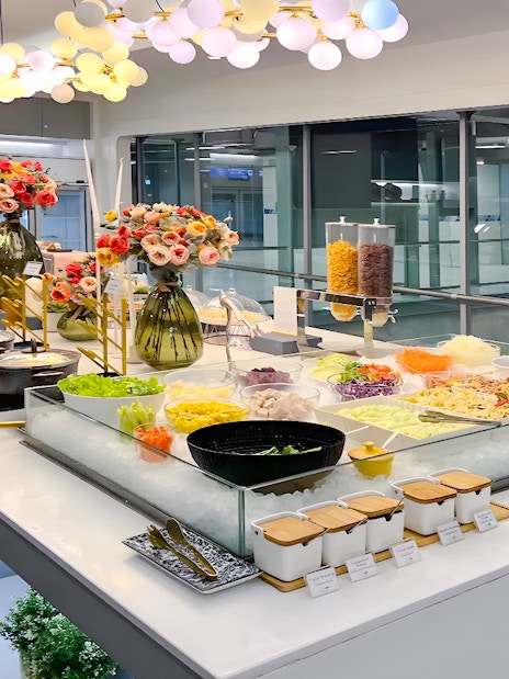 Buffet spread at Coral Finest Business Class Lounge, Bangkok airport, featuring salads and hot dishes.