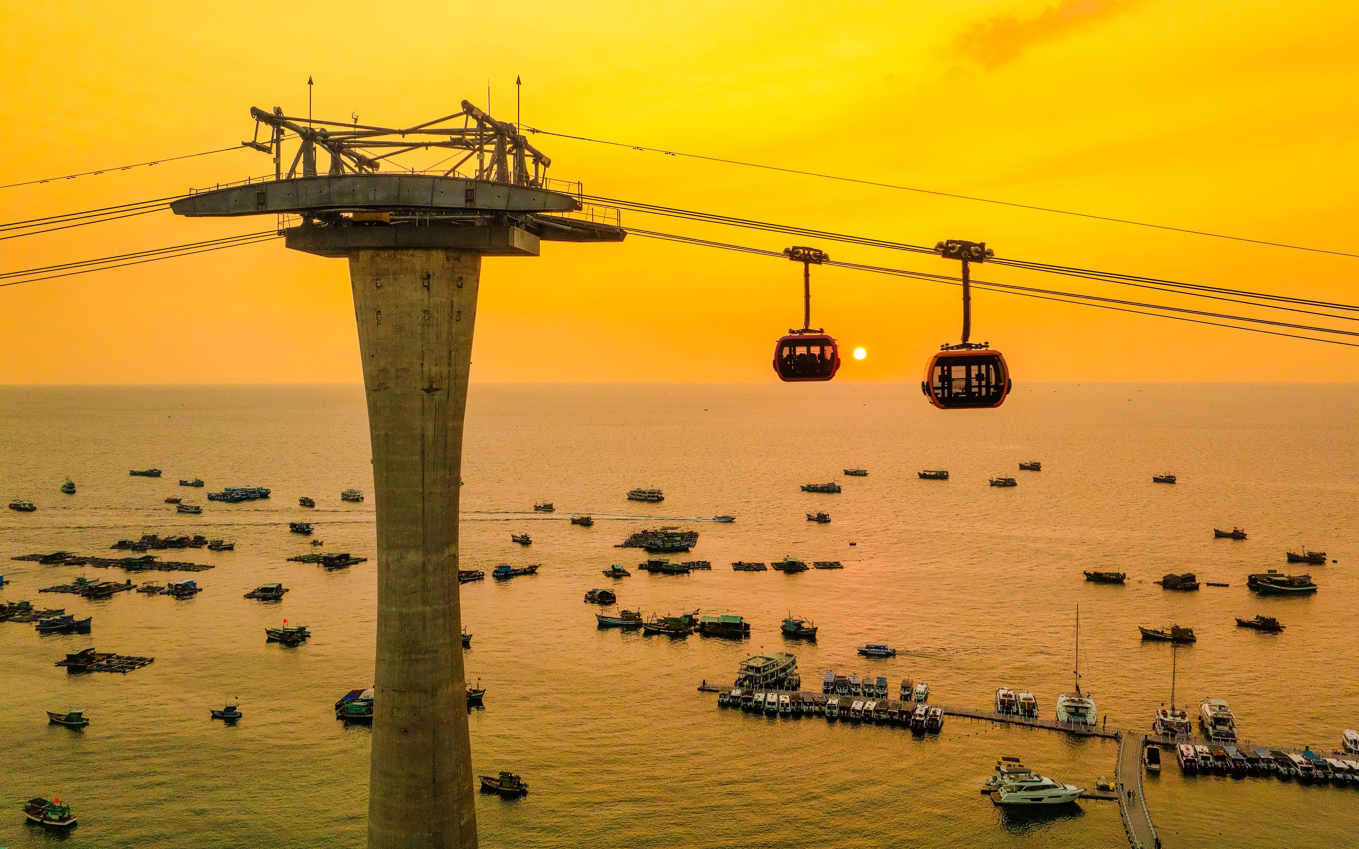 Cable cars over ocean at sunset, Phu Quoc island, Vietnam, with boats below.