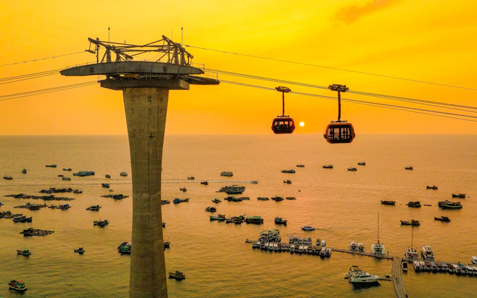 Cable cars over ocean at sunset, Phu Quoc island, Vietnam, with boats below.