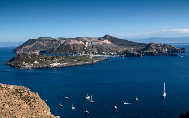 Sailboats near Vulcano Island with volcanic landscape in the background.