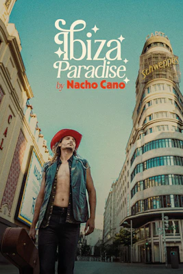 Man in red hat and vest stands on Madrid street with Schweppes building, promoting Ibiza Paradise by Nacho Cano show.