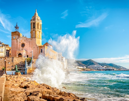 Church of Sant Bartomeu and Santa Tecla with waves crashing in Sitges, near Barcelona.