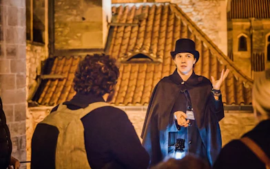 Tour guide in historical attire leading Ghosts & Legends of Old Town Prague tour at night.