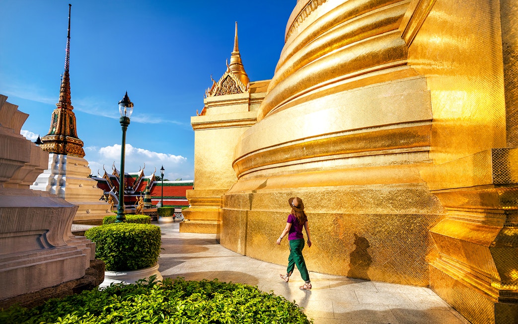 Woman walking near golden stupa at Wat Phra Kaew, Bangkok.