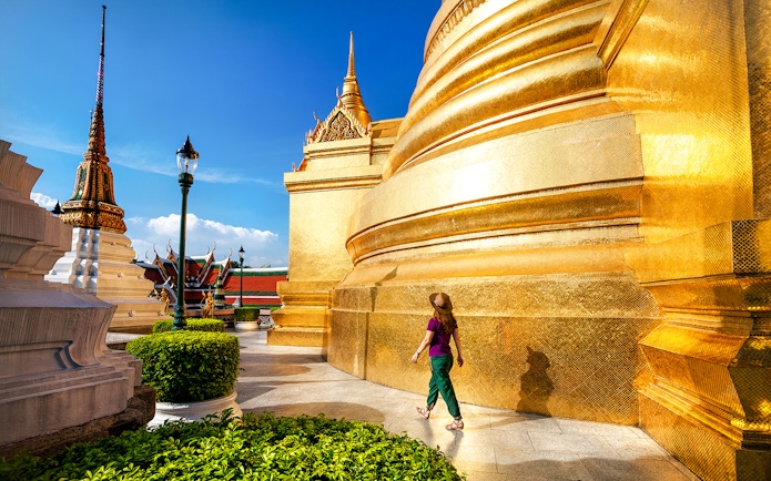 Woman walking near golden stupa at Wat Phra Kaew, Bangkok.