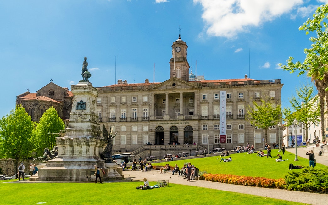 Stock Exchange Palace and Don Henrique Statue in Porto, Portugal, with people relaxing on the lawn.